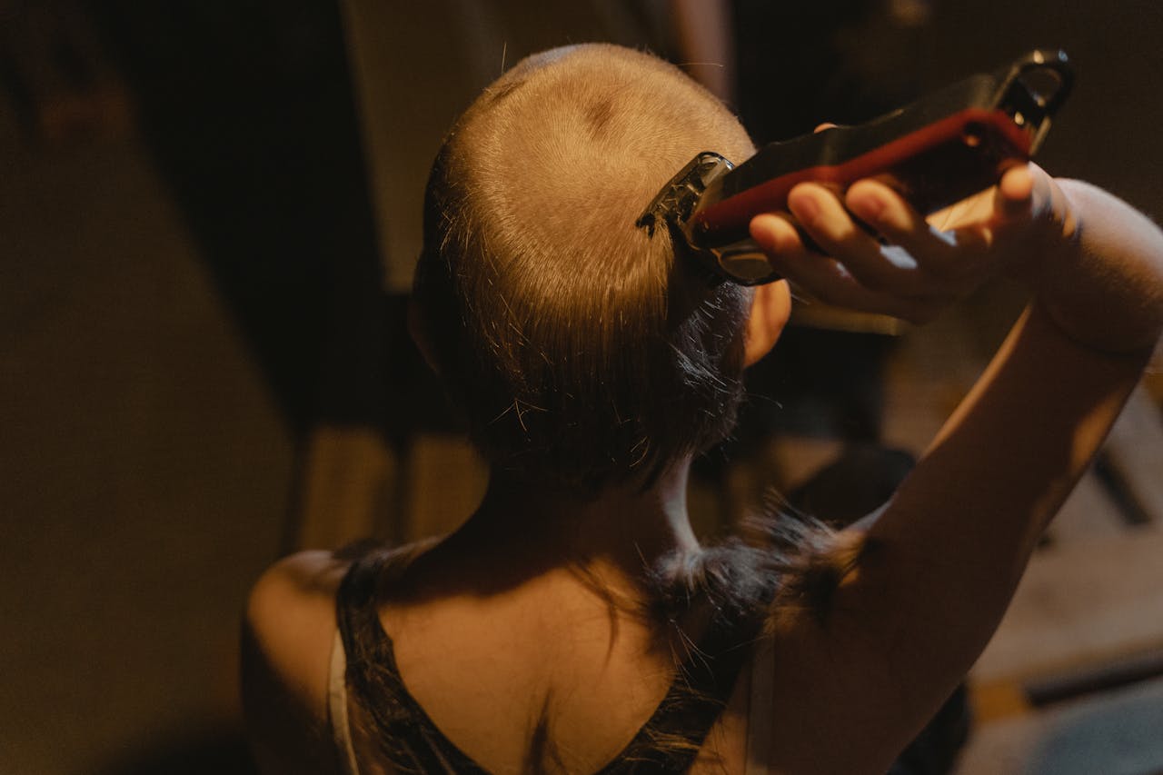 why-choose-us Top view of woman shaving her head with an electric clipper indoors.
