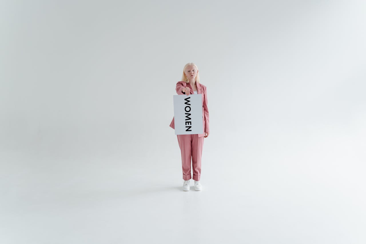 portfolio-01 A woman in a pink suit holds a 'Women' sign, symbolizing empowerment in a minimalist studio.